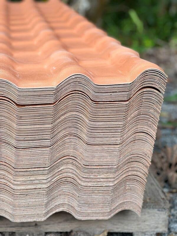 Pilha de telhas de PVC colonial PERMATTI em tom cerâmica. Vista em detalhe das camadas e ondulações, destacando a leveza e resistência do material para as coberturas.