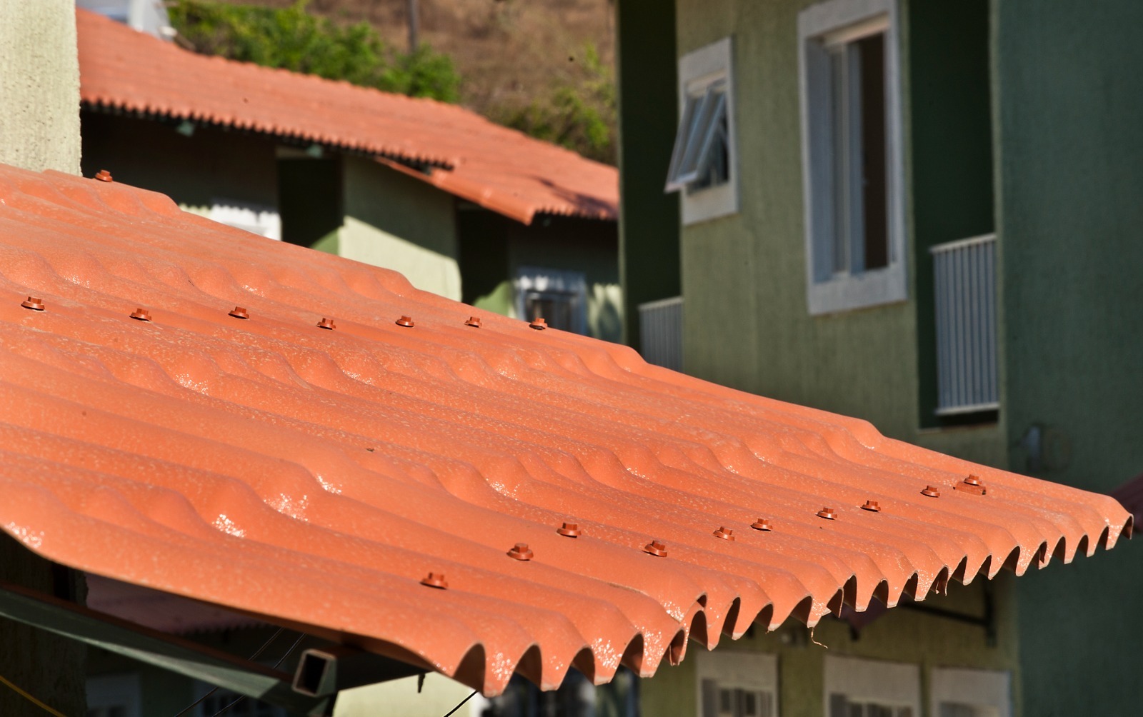 Telha ondulada Permatti terracota com parafusos visíveis. Ajuda a responder qual telha esquenta menos, promovendo isolamento térmico e conforto em prédios ao fundo.
