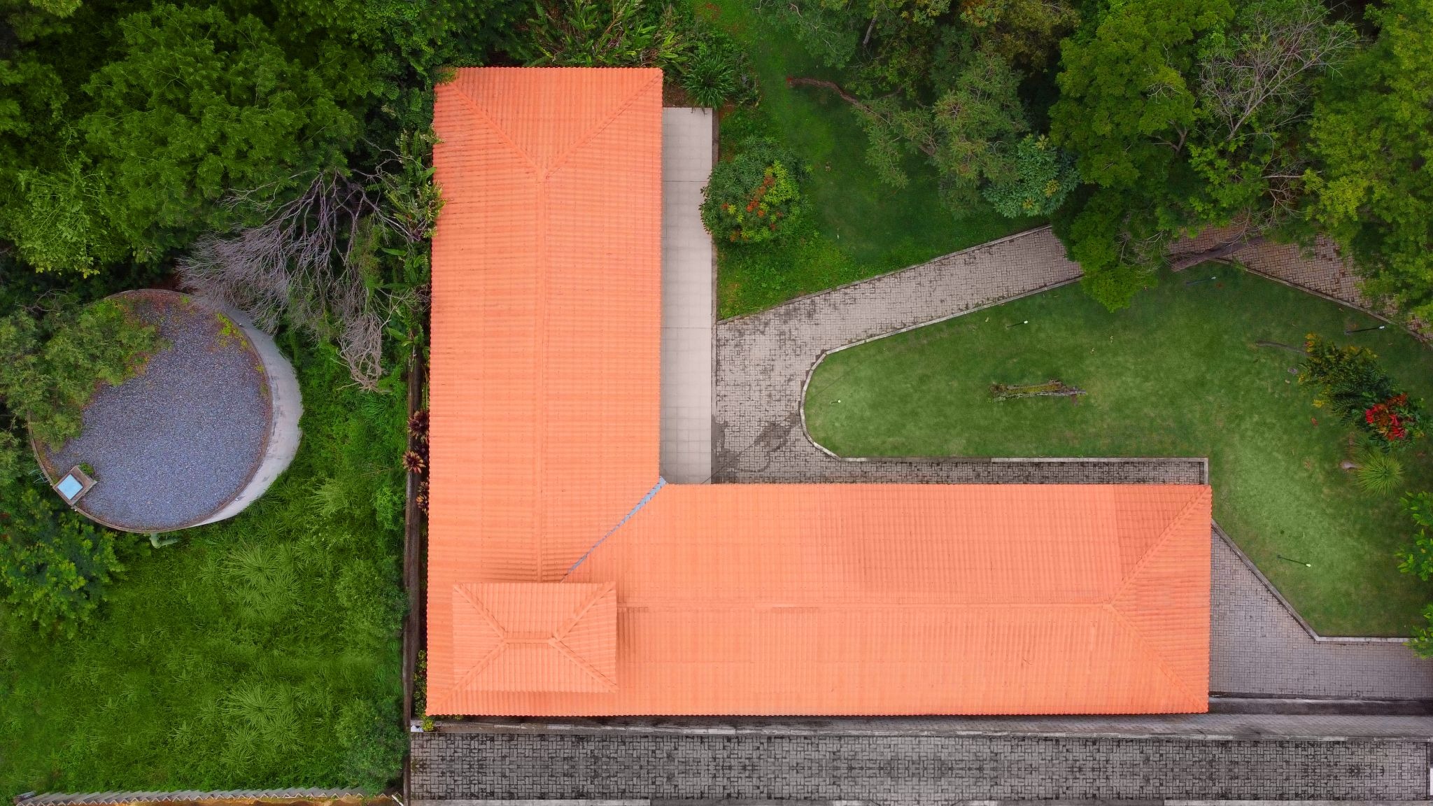 Vista aérea de telhado L terracota, ideal para garagens Permatti. Mostra telhas, caminhos de pedra, grama e árvores ao redor da casa.
